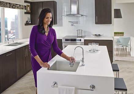 A woman in purple dress standing at the sink.